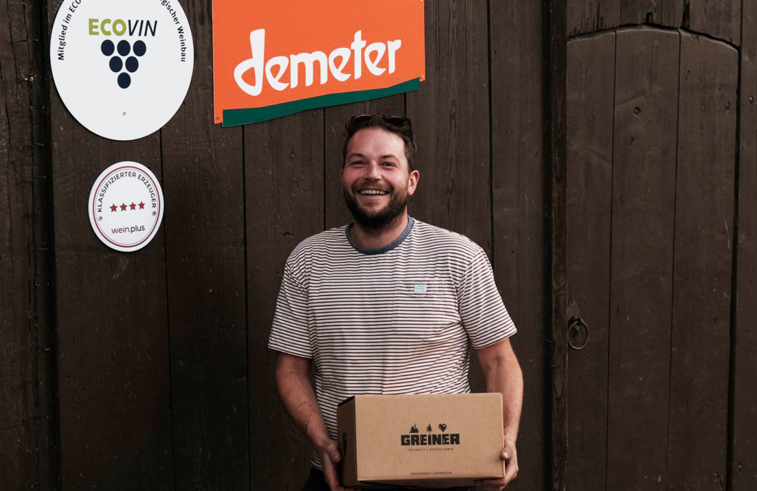 Max holding a case of wine below a Demeter sign at the winery