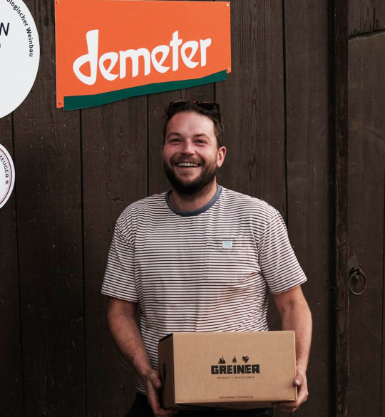 Max holding a case of wine below a Demeter sign at the winery